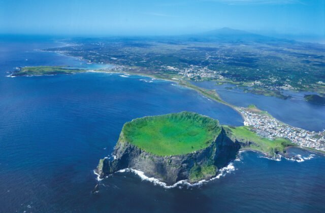 城山日出峰火山口自海面升起、遠方為漢拏山