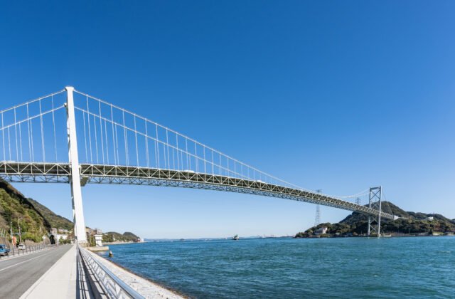 橫跨關門海峽的關門橋吊橋，連接本州的下關與九州的門司，襯著藍天與海