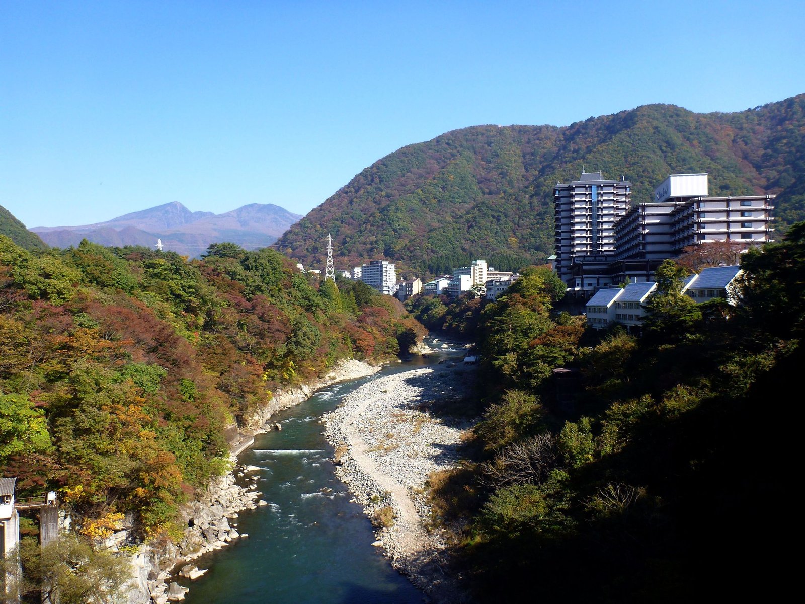秋季從橋上眺望鬼怒川溪谷，兩岸紅葉與溫泉飯店林立，遠方可見群山